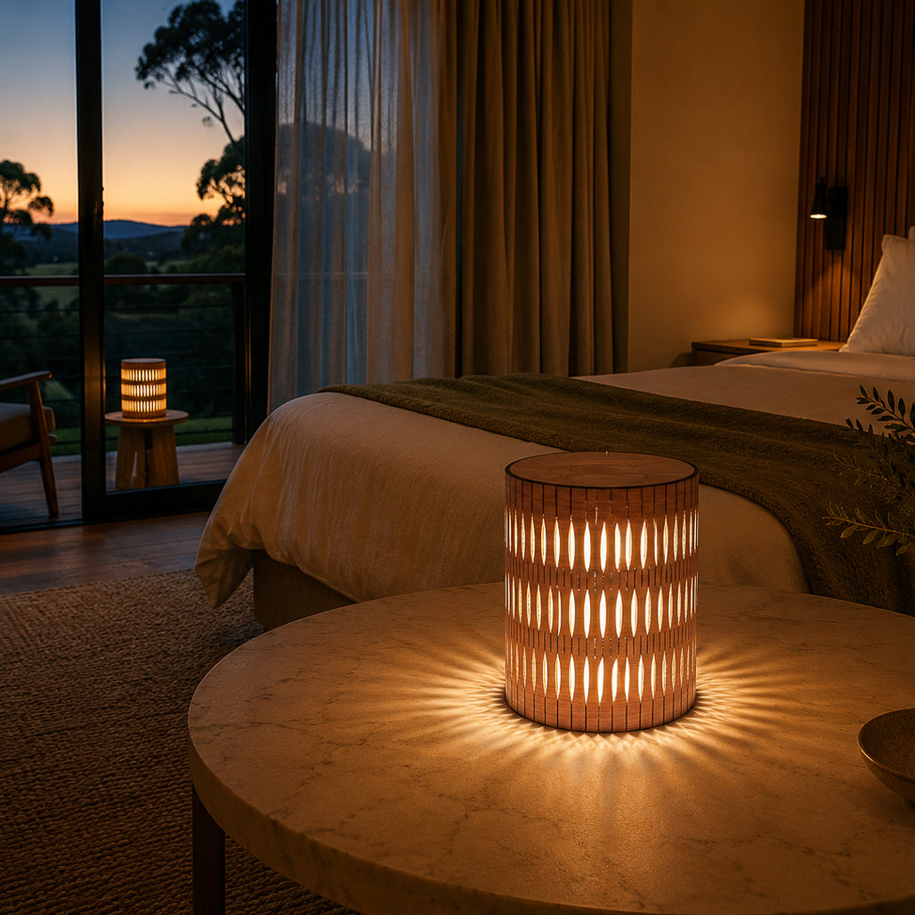 Luminous woven table lamp on a round wooden table with a bedroom setting and sunset view.