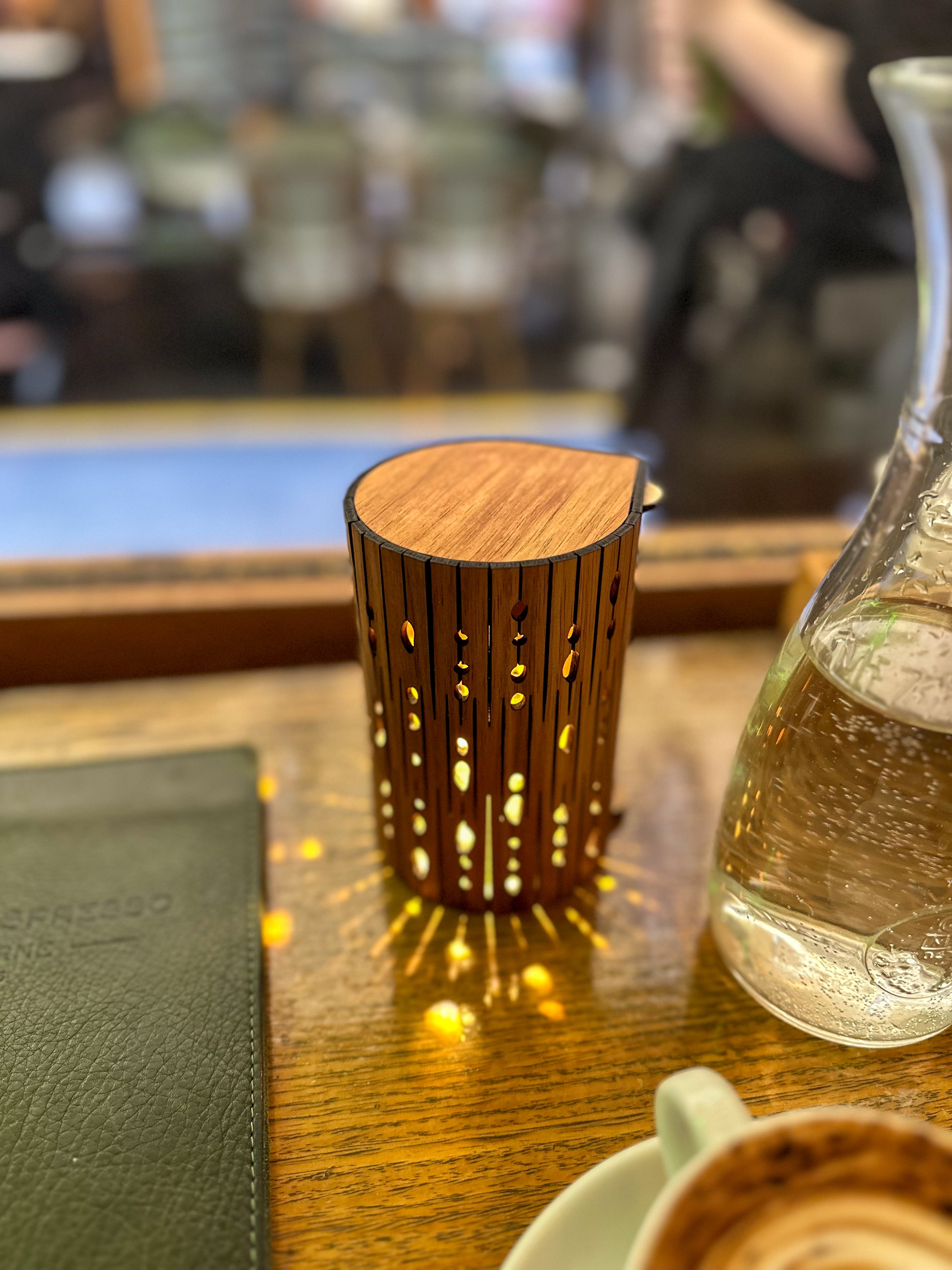 Wooden candle holder casting warm light on a café table beside a glass carafe and coffee cup