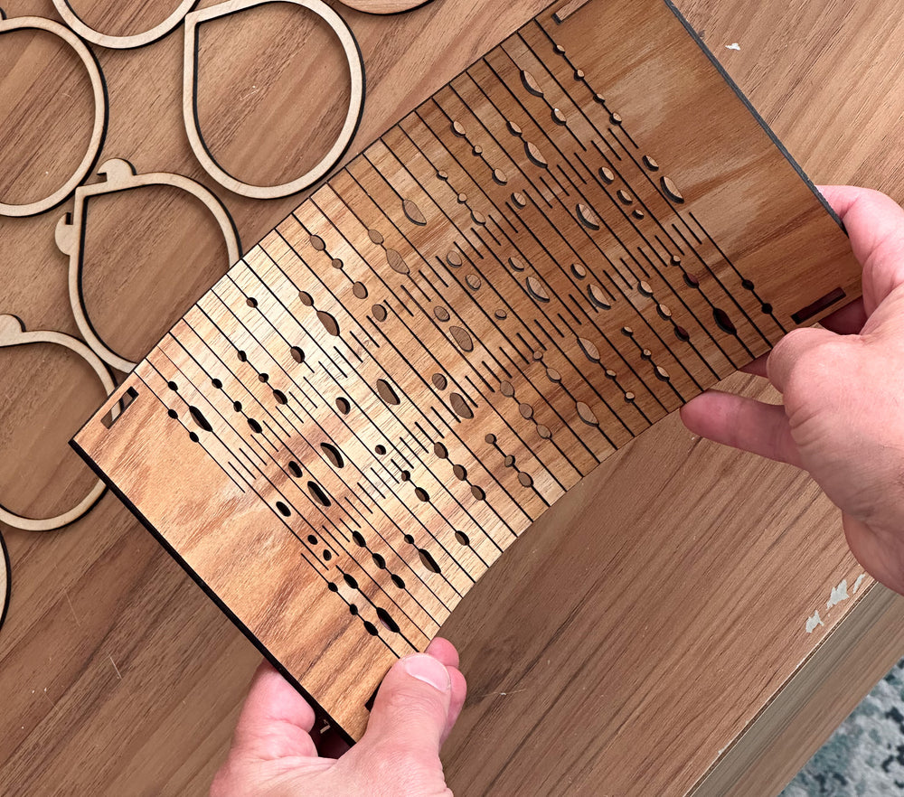Wooden frame piece with laser-cut patterns held by a hand on a wooden surface.