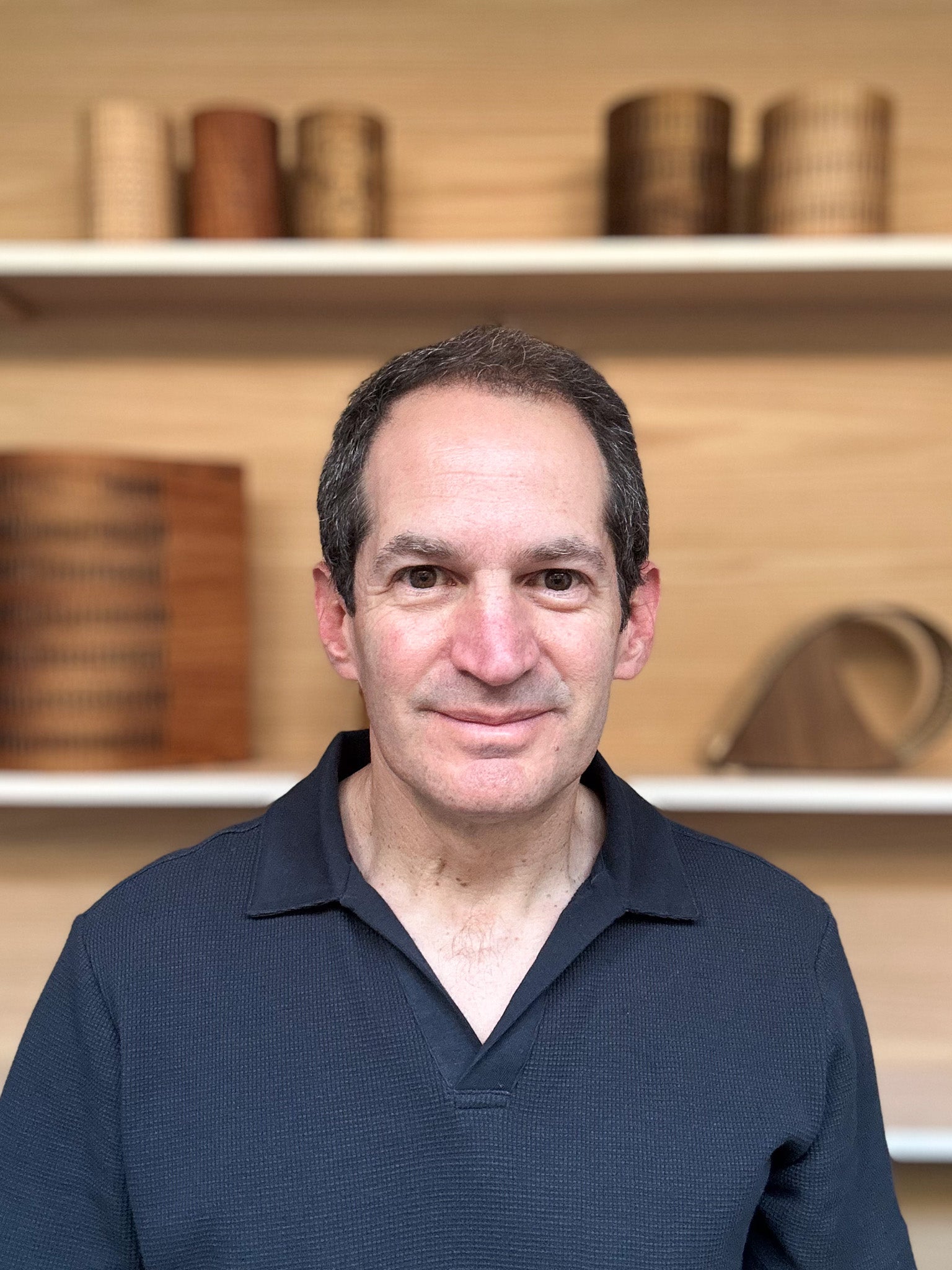 Man wearing a dark blue shirt in front of shelves with wooden items