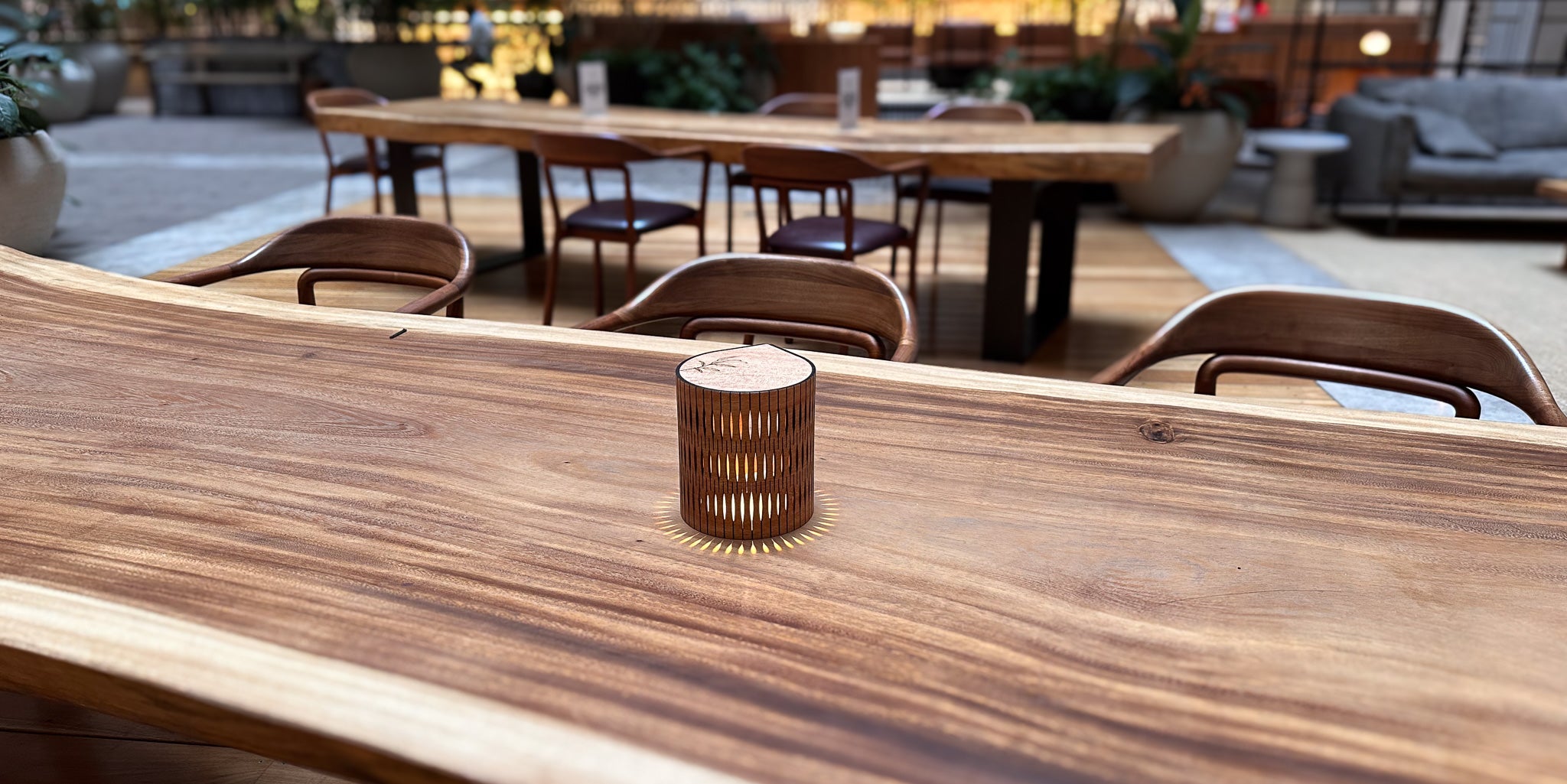 Wooden table with a wooden lamp on it, set against an outdoor cafe background.
