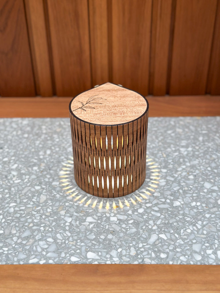 Wooden cylindrical lamp with engraved botanical on a gray surface