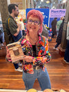 Woman with pink hair holding a wooden item in a busy indoor setting
