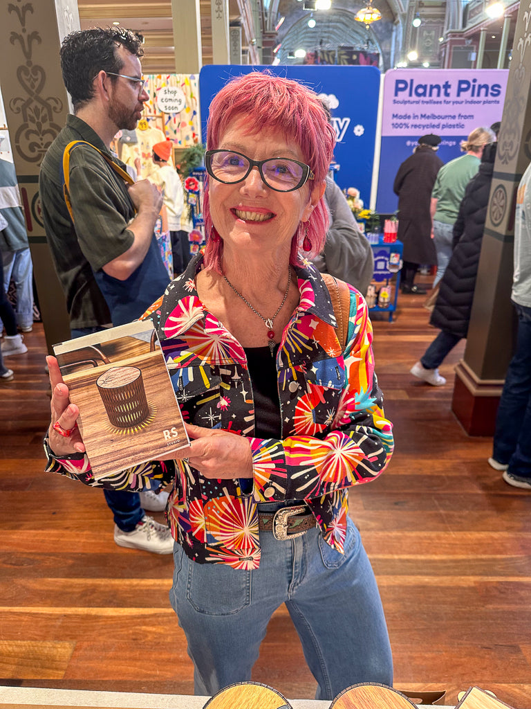 Woman with pink hair holding a wooden item in a busy indoor setting