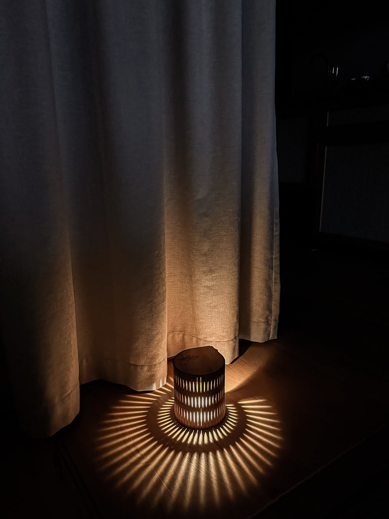 Wooden Portable Bubble Lamp casting a shadow on a dark floor with a light curtain in the background