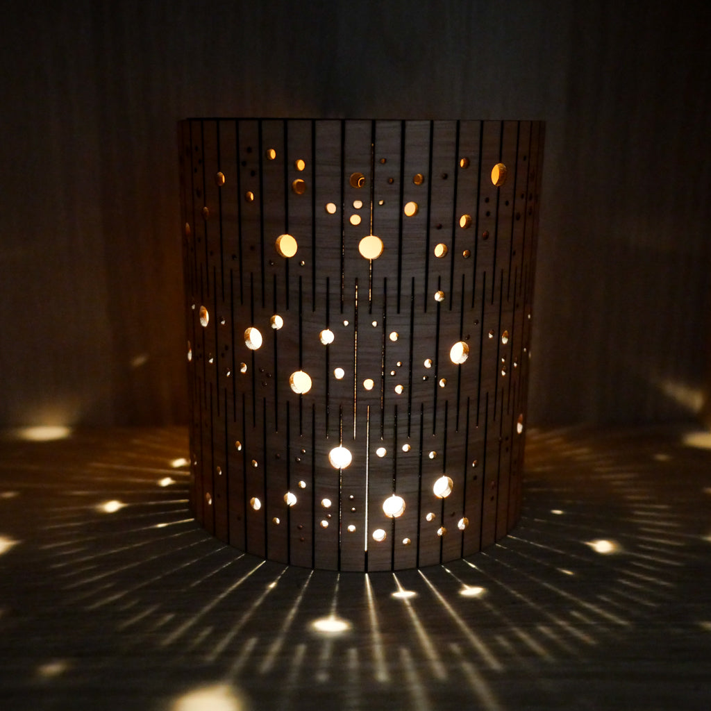Timber bubble lamp with circular cutouts casting celestial shadows on a dark background