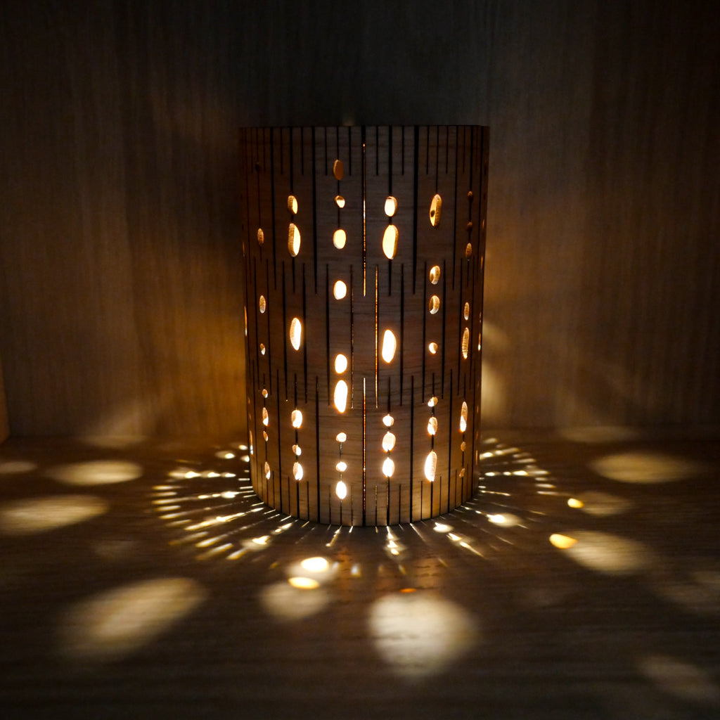 Timber cafe lamp with organic cutouts casting dappled botanical shadows on a dark background