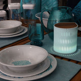 Dining table setting with white bowls, blue glasses, and RS Studio bubble lamp in mint green on a wooden surface.
