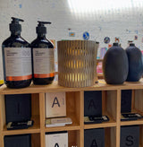 Two black bottles with labels on a wooden shelf, with decorative items including vases and RS Studio bubble lamp.