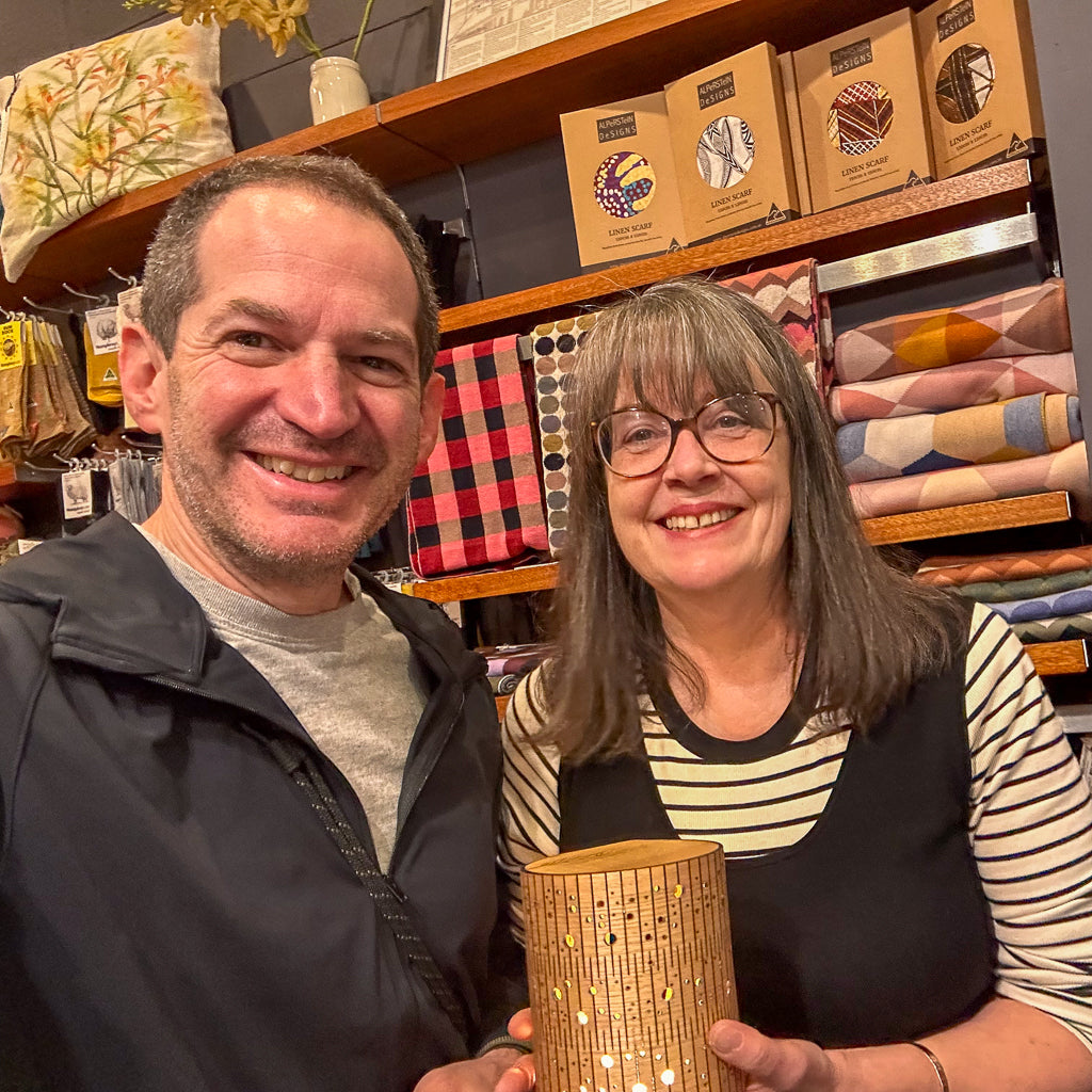 Man and woman holding a wooden bubble lamp in a store with shelves of fabric in the background