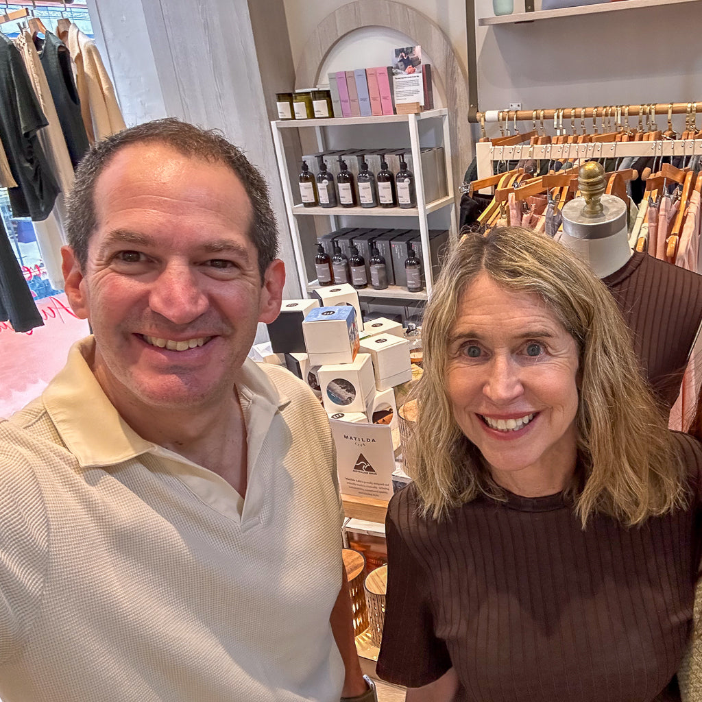 Two people posing for a selfie in a Matilda Life store with shelves and clothing racks in the background.