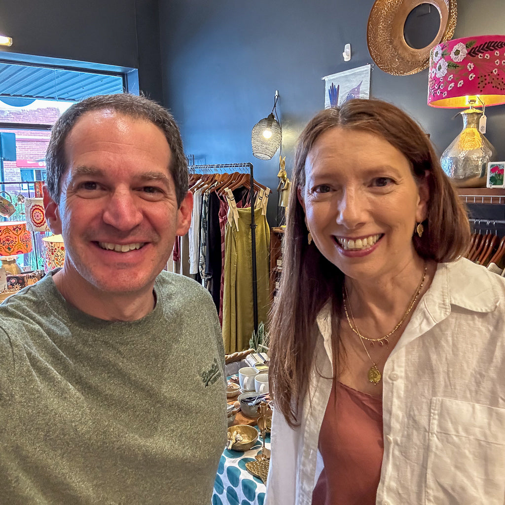Two people smiling in a store with clothing and decor items in the background
