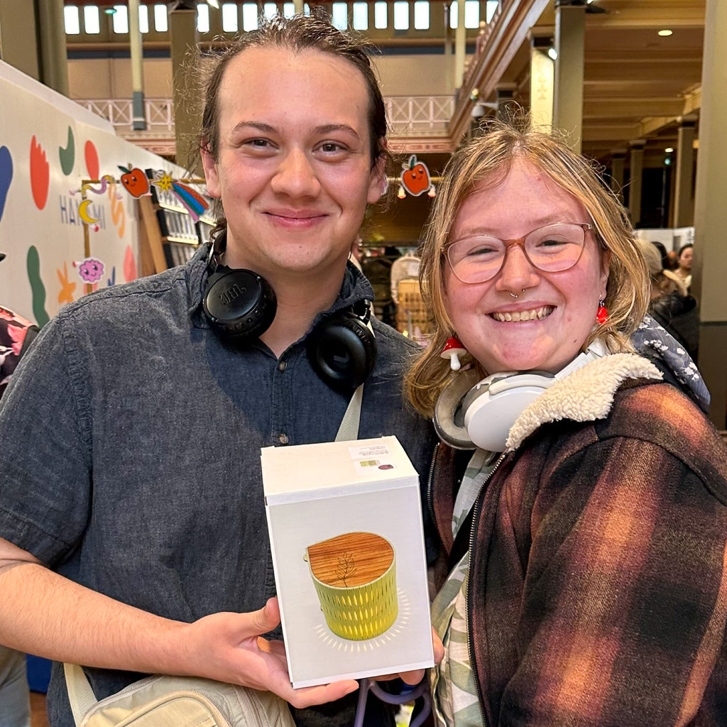 Two people holding a banksia green bubble lamp, standing in a market