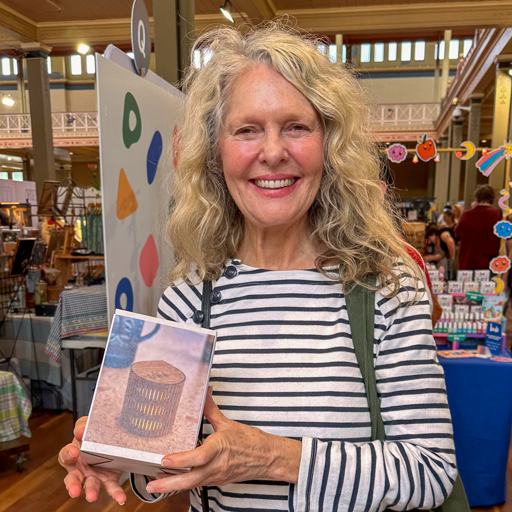 Woman holding a eucalypt bubble lamp, standing in a market with tables and chairs.